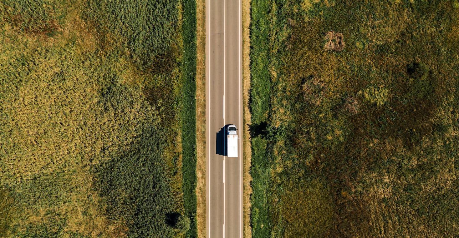 An overhead shot of a truck on a last-mile delivery driving through a woodland plain area.